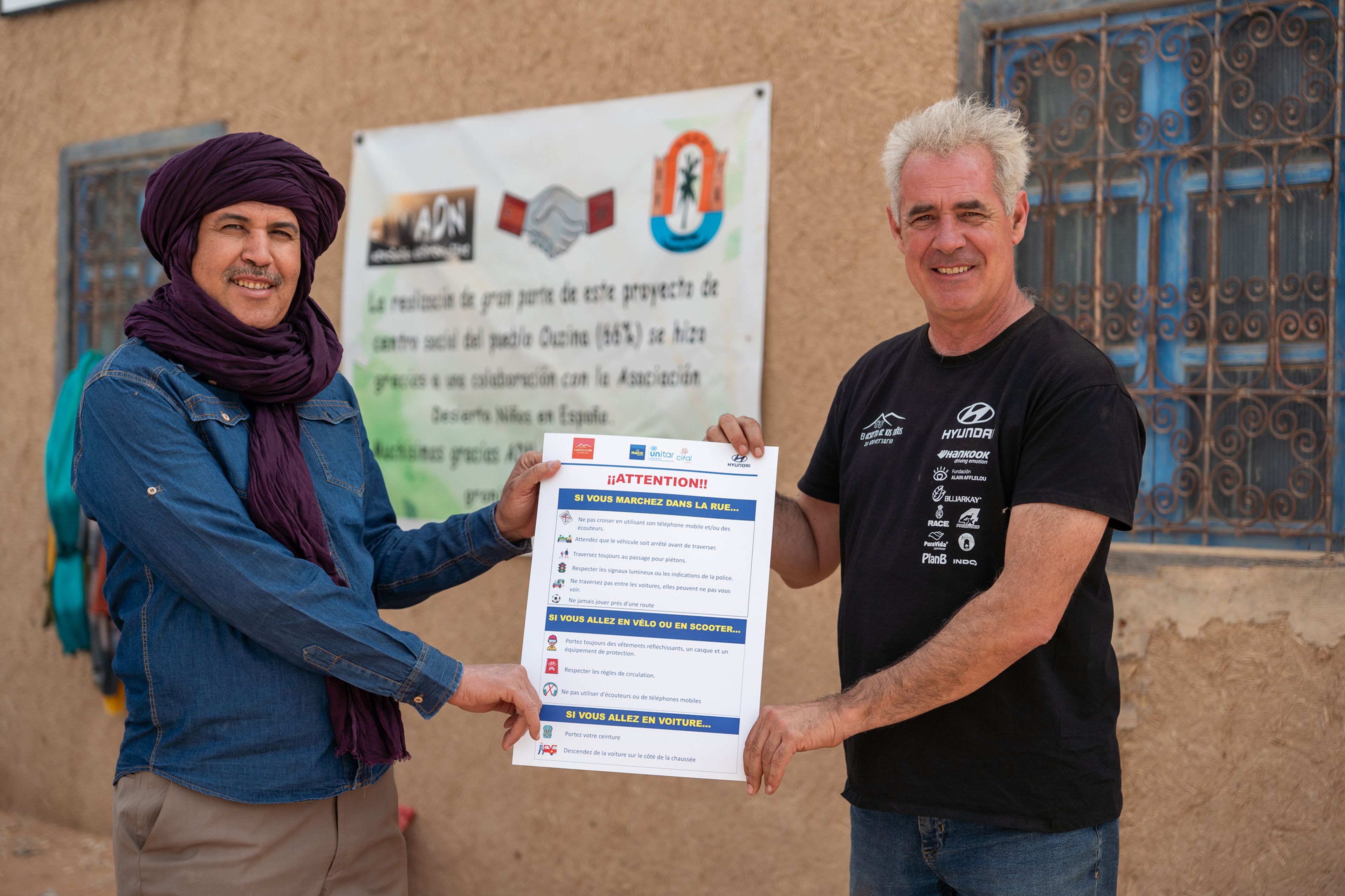 Nacho Salvador (derecha) es el creador de 'El desierto de los niños. Aquí hace entrega de un díptico con indicaciones de seguridad vial (elaborado por el RACE) al profesor de la escuela de Ouzina (Marruecos).